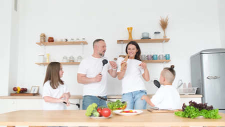 Funny young couple singing and dancing in the kitchen, using spoons instead of a microphone.の写真素材