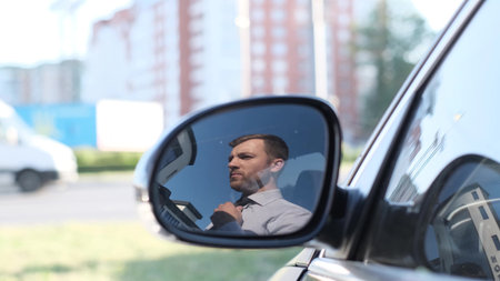 Young businessman man puts on a tie on the street, looking out the window of his car.