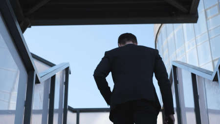 Businessman with a briefcase in his hands climbs the stairs, rear view. The man goes to the officeの写真素材