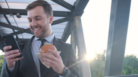 Young manager eating fast food during lunch break outdoors, on the way to work. Harmful street foodの写真素材