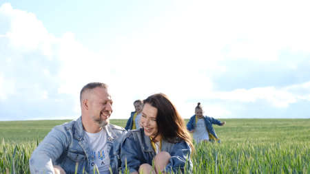Cheerful family walks through a green field of wheat. Parents hold children by the hands.の写真素材