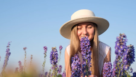 A young woman of European appearance in a white hat sniffs lavender flowers in the middle of a lavender fieldの写真素材