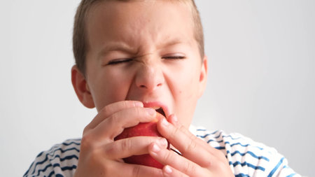 Beautiful baby boy bites a peach. The face of a child eating a healthy snack, ripe fruit.の写真素材