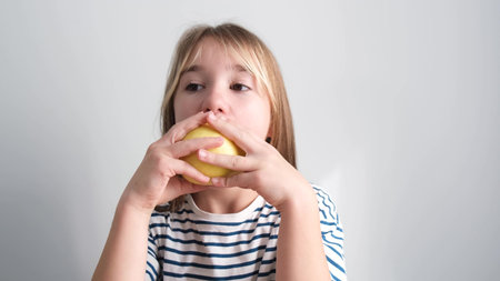 A little girl with fair hair is eating a juicy pear. Childrens breakfast in the kitchen at homeの写真素材
