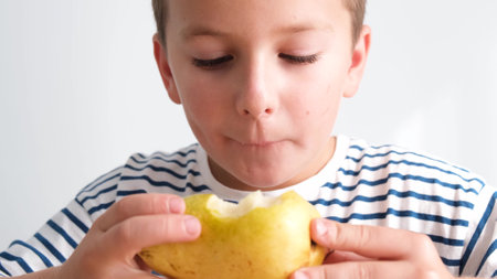 Portrait of a cute little boy against a white wall eating a juicy pear. High quality 4k videoの写真素材