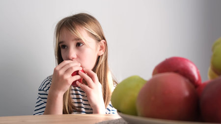 Child girl blonde eats an apple on a white background. Video Delicious ripe autumn fruits