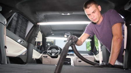 Male worker removing dirt from car seat with professional vacuum cleaner.の写真素材