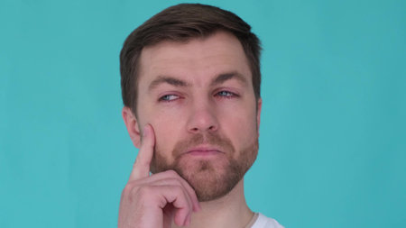 Close up portrait of pensive man on turquoise background in studio. Guy thinking touching chinの写真素材