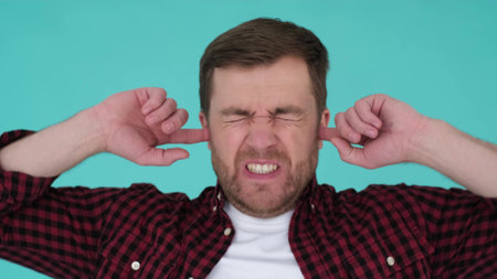 Angry man shouting and covering his ears with his hands isolated on a turquoise in the studioの写真素材