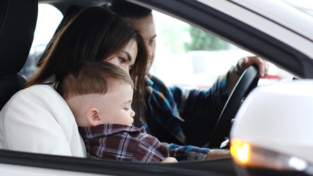 A husband, wife and little son are sitting in a new car. The joy of a new purchase.