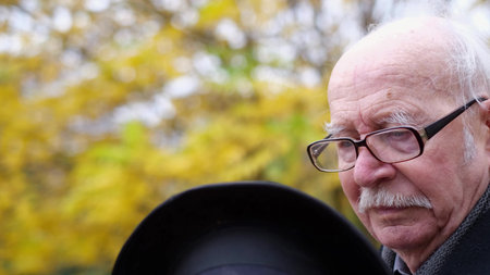 Gray-haired old retiree puts a hat on his head, he is resting in the autumn park
