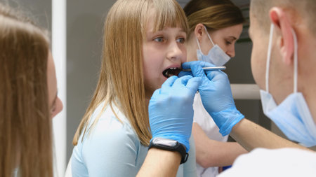 A dentist and his assistants examine the oral cavity of a red-haired teenage girl. assistantsの写真素材