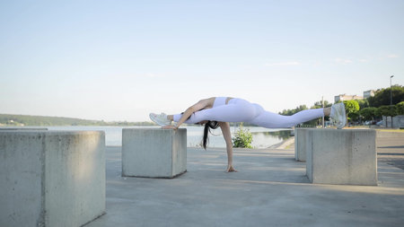 A young athlete does gymnastics on the shore of the lake. Sporty women do yoga on the street.