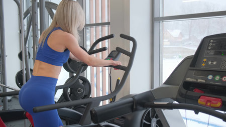 A young sporty woman works out on an elliptical machine in the gym, does cardio.