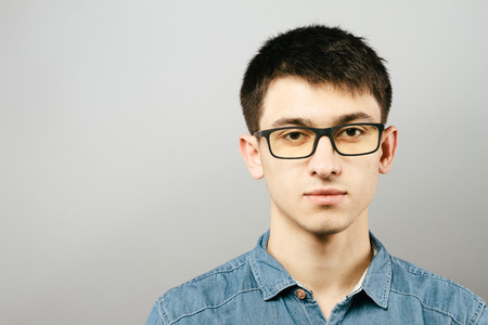 Close up Smiling Young Businessman Wearing Eyeglasses, Looking at the Camera Against Gray Wall Background with Copy Spaceの写真素材