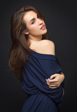 girl in blue peignoir with bare shoulder. Dark background. Cute smile. The concept portrait in the studio.の写真素材