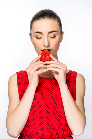 Beautiful girl in a dress with perfect smile eating red strawberry. Healthy food. Isolated on white. a model light nude make-up, gray studio background, beauty photo, close .の写真素材