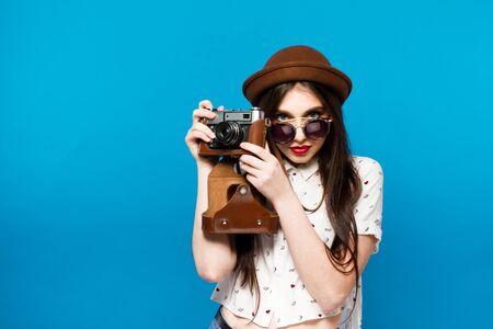 Beautiful girl in brown hat and round sunglasses holding old camera.の写真素材