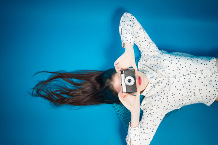Cheerful girl lying on the floor with her camera in hands.の写真素材
