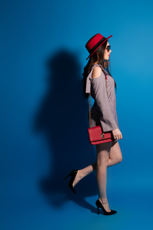 Lovely model in fashionable red Hat and a red Clutch on blue backgroundの写真素材