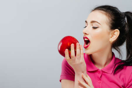 Beautiful young woman eating a red apple. Isolated over white.の写真素材