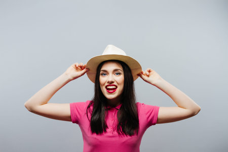 Cheerful girl holding the brim of her hat and laughing at camera in summer