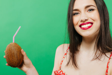 Portrait of Toothy Smiling Young Woman Drinking Tropical Cocktail in Coconut and Looking at the Camera on Green Background.の写真素材