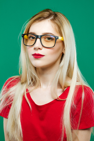 Wonderful Portrait of Cute Smart Girl in Eyeglasses and Red Top. Studio Short of Beautiful Blonde on Green Background.の写真素材