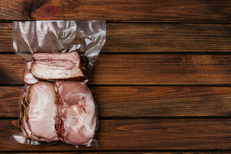 Smoked meat, sliced and packed in a vacuum package, closeup. Wooden background.の写真素材