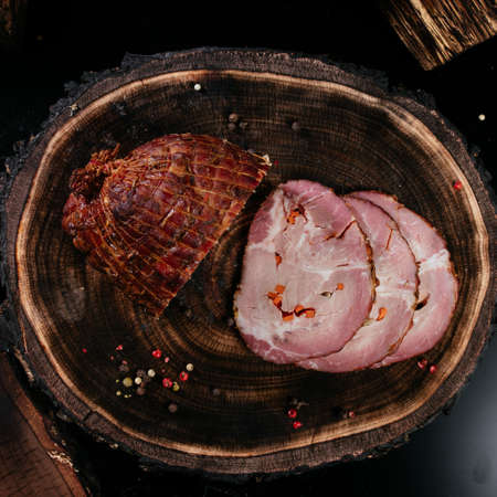Freshly smoked piece of pork dog, sliced, laid out on a wooden background with oak stump. Close-up. High quality photoの写真素材