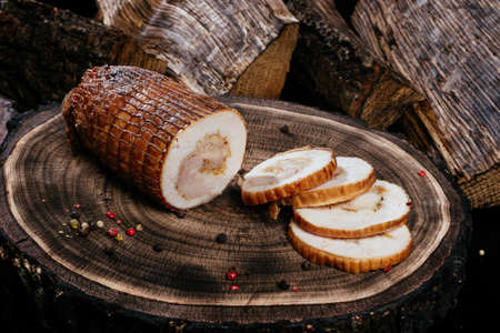 Freshly smoked piece of pork dog, sliced, laid out on a wooden background with oak stump. Close-up. High quality photoの写真素材