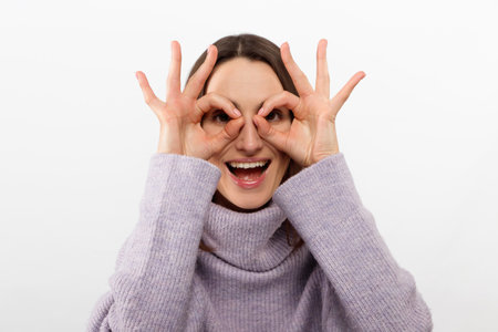Close up shot of young positive woman with long hair looking at camera through ok-gesture, Beautiful...