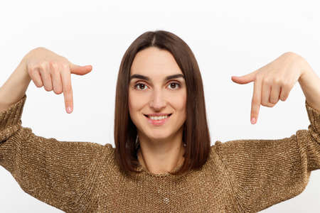 young nice girl showing down in a golden sweater on a white background conceptual promotional photoの写真素材