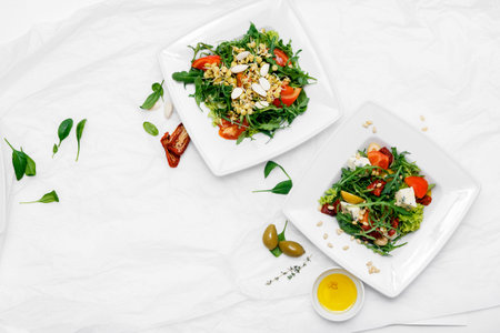 Healthy food. Two white plates. Tomato salad, arugula, spinach, olives, pepper on White background