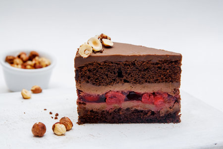 a piece of chocolate cake with cherries and hazelnut on white background. Delicious chocolate cakes on table close-upの写真素材