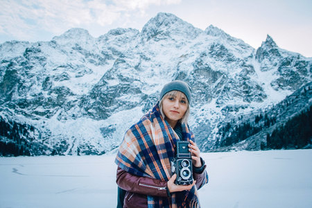 Beautiful girl makes a photo on an old vintage camera. In the mountains in winter, adventure and...