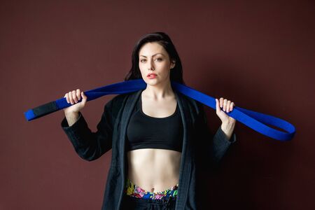 Portrait beautiful athletic woman in black kimono with blue belt. Martial arts concept. Indoor, studio shot, background with copy space advertisingの写真素材