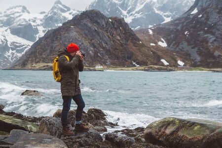 Traveler professional photographer taking nature photo of landscape. Wearing a red backpack wearing a red hat standing on rocks against the background of the sea and the mountains. Travel lifestyle concept.の写真素材