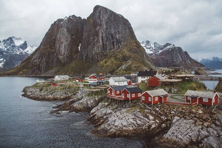 Classic and beautiful landscape of the Lofoten Islands with red fishermens houses in front of the sea and high mountains in the background, Northern Europe, Norwayの写真素材