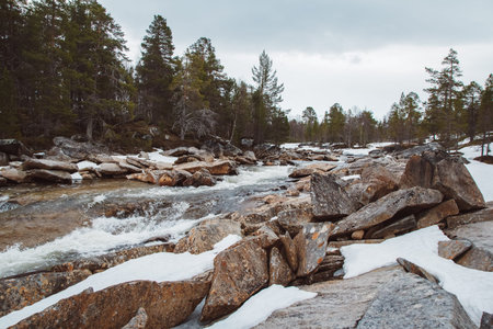 Landscape of the mountain river and the waterfall flowing between the snow-covered rocks and the...