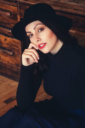 Portrait of a beautiful brunette woman in a hat on the background of a wooden table. Positioning female portrait. A look at the cameraの写真素材