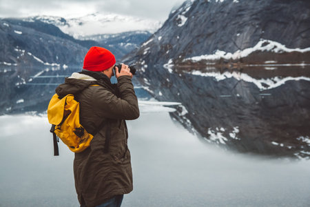Traveler man with a yellow backpack wearing a red hat standing on the background of mountains and...