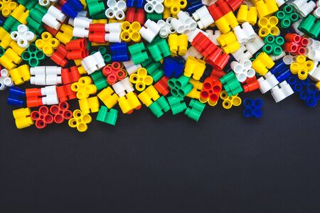 Multicolored plastic blocks on a black background with a place for text. Parts of the bright little spare parts for toys. Top view.の写真素材