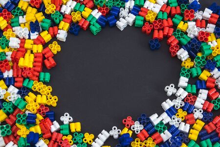 Multicolored plastic blocks on a black background with a place for text. Parts of the bright little spare parts for toys. Top view.の写真素材