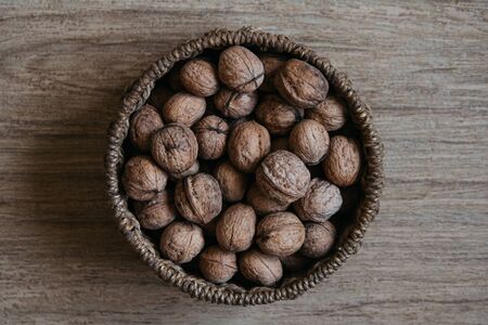 Walnuts in a round wicker basket on a wooden background. Top view. Central compositionの写真素材