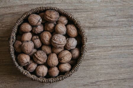 Walnuts in a round wicker basket on a wooden background. Top view. Copy, empty space for textの写真素材