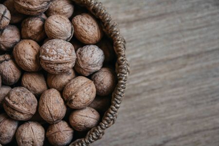 Walnuts in a round wicker basket on a wooden background. Top view. Copy, empty space for textの写真素材