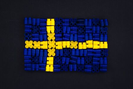 Colorful plastic bricks which form the Sweden flag on black paper background. Parts of bright small spare parts for toys. Top viewの写真素材