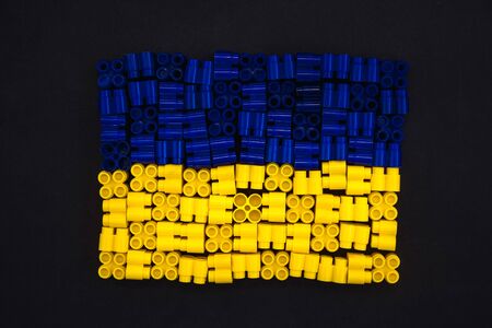 Colorful plastic bricks which form the Ukraine flag on black paper background. Parts of bright small spare parts for toys. Top viewの写真素材