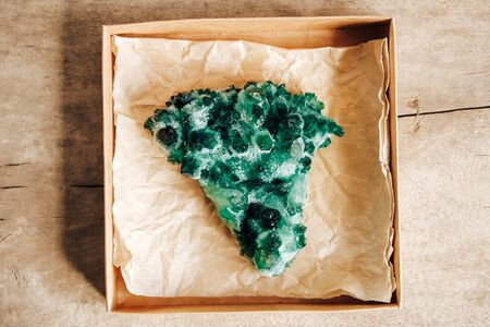 Raw emerald and gemstone rough rock crystal in a kraft paper box on wooden background. Top view. Copy, empty space for text.の写真素材